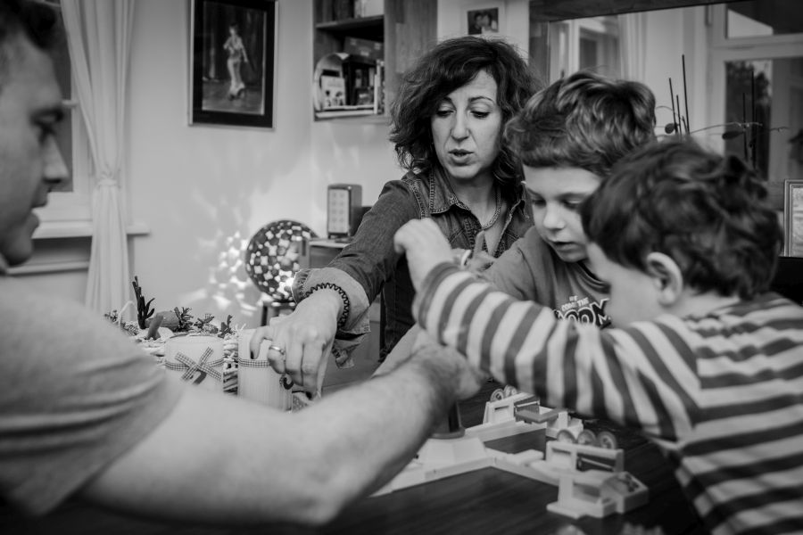 Mutter, Vater und zwei Söhne spielen zusammen ein Brettspiel und greifen alle gleichzeitig und gespannt auf das Spielbrett.