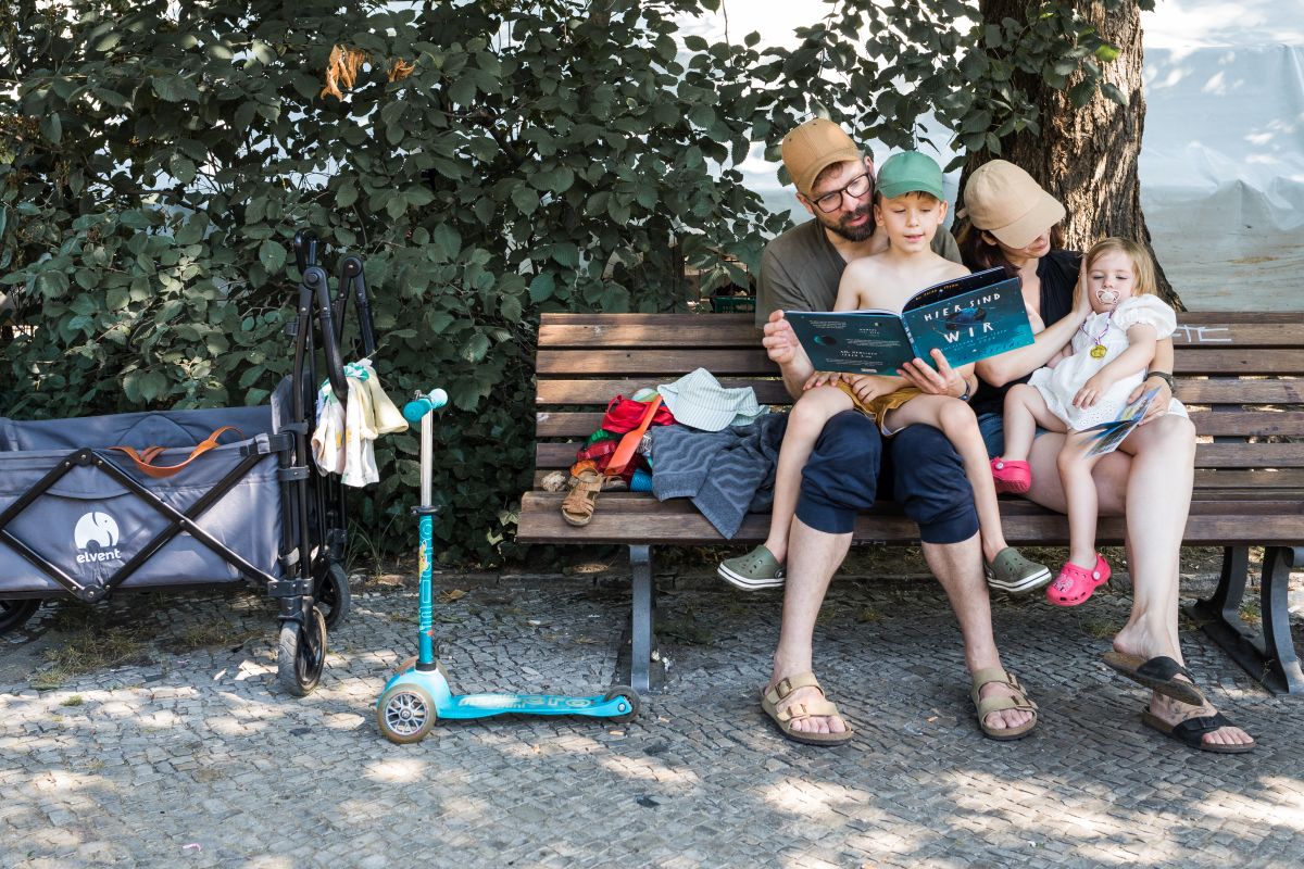 Eine vierköpfige Familie sitzt auf einer Parkbank. Jeder ist mit sich beschäftigt, aber alle sind zusammen.