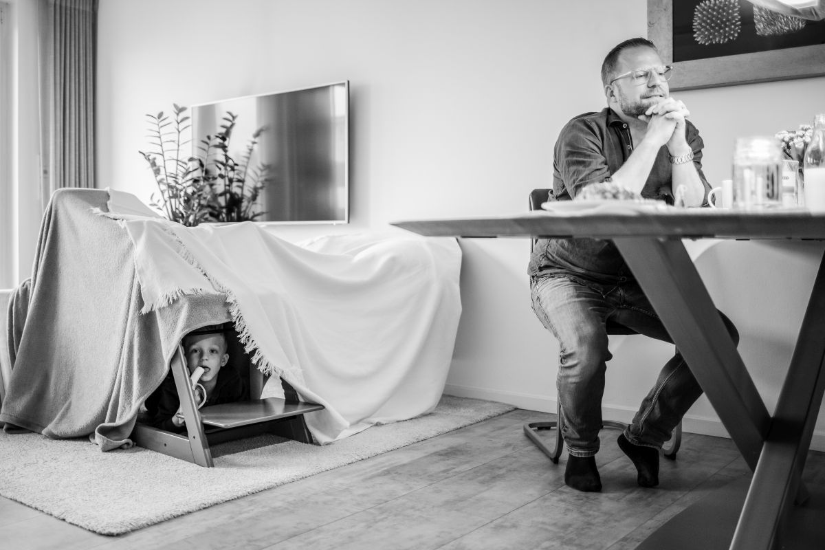 Ein Junge schaut aus einer Öffnung seiner aus Decken und Stühlen gebauten Höhle heraus. Dabei isst er eine Banane.