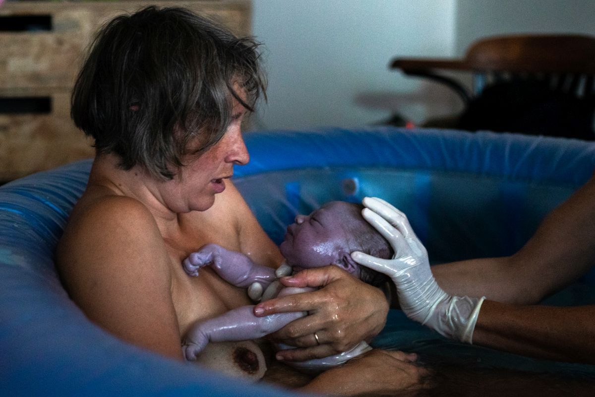 Die Hebamme gibt der frisch gebackenen Mutter zum ersten Mal das Neugeborene in den Arm.