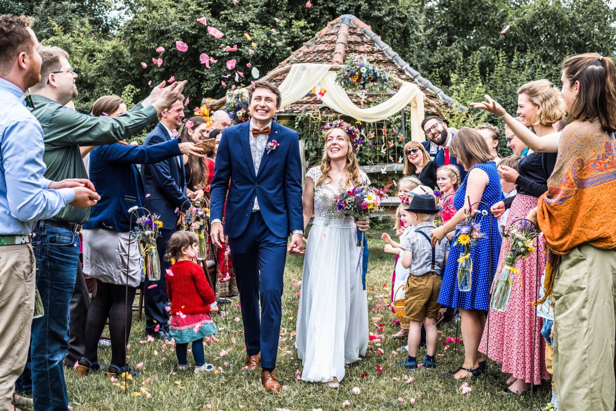 Brautpaar beim Auszug auf einer Wiese. Links und rechts von ihnen werfen ihre Gäste mit Blumenblüten.