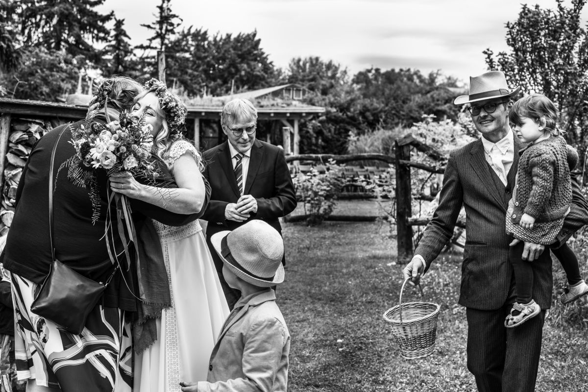 Umarmung der Braut durch Hochzeitsgäste. Drum herum andere fröhliche Gäste.