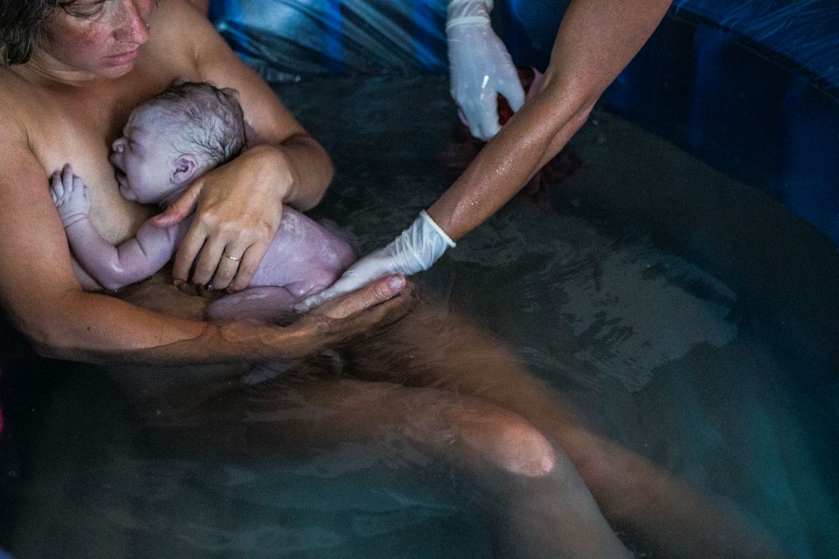 Eine Frau im Gebärpool nimmt ihr Neugeborenes entgegen.