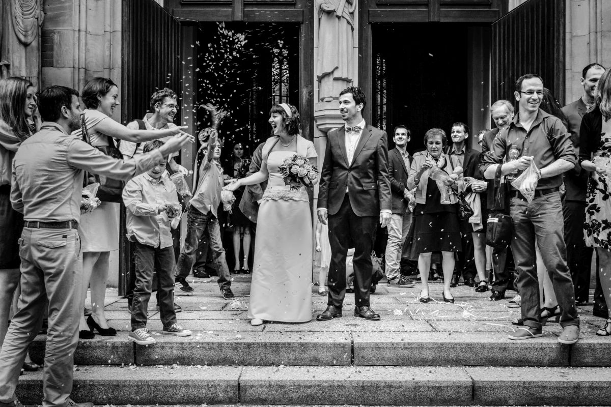 Ein Hochzeitspaar verlässt eine Kirche in Berlin und wird von ihren Gästen festlich empfangen.
