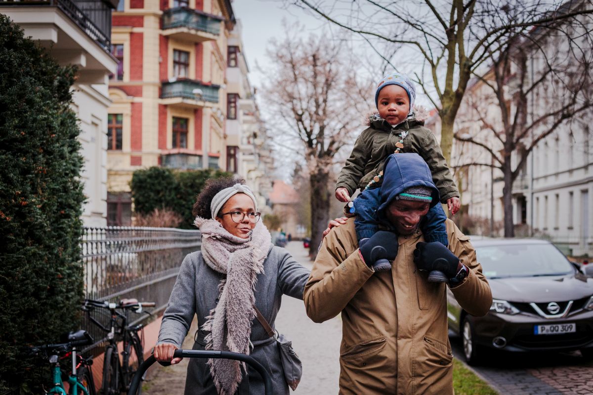 Ein Elternpaar spaziert durch Potsdam West. Beide Eltern lachen. Die Mutter berührt den Vater liebevoll an
                                der Schulter. Der Vater trägt den kleinen Sohn auf den Schultern.